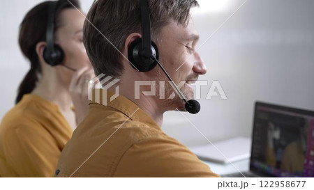 Focused male call center operator in yellow casual shirt is assisting clients online, providing customer support and answering inquiries. Call center operators Focused male call center operator in yellow casual shirt is assisting clients online, providing customer support and answering inquiries. Call center operators 122958677