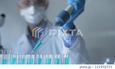 Woman scientist researcher using a micropipette to fill up test tubes with a blue liquid in laboratory setting, closeup view. Medicine and science concept 122958725
