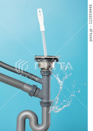 Drain sink leak water from pipe plumbing in kitchen bathroom as water splash clogged drop. Pouring Leaking water from gray plastic pipe drain sink by probe cable. Blue background isolated Drain sink leak water from pipe plumbing in kitchen bathroom as water splash clogged drop. Pouring Leaking water from gray plastic pipe drain sink by probe cable. Blue background isolated 122959948