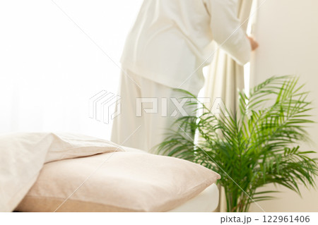 朝の寝室でカーテンを開けるパジャマ姿のミドル女性 朝の寝室でカーテンを開けるパジャマ姿のミドル女性 122961406