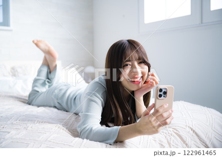 スマホでを持つ寝転ぶカメラ目線の女性 全身 スマホでを持つ寝転ぶカメラ目線の女性 全身 122961465