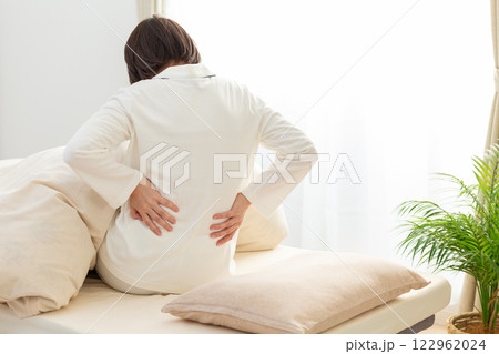 朝の寝室で腰痛に苦しむ白いパジャマ姿のミドル女性 朝の寝室で腰痛に苦しむ白いパジャマ姿のミドル女性 122962024