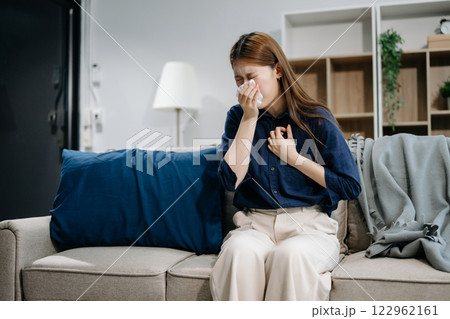 Young Asian woman suffering from flu symptoms, covered with a blanket on a sofa. Concept of illness, healthcare 122962161