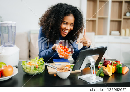 Smiling woman in a modern kitchen with fresh fruits, vegetables, blender, and orange juice, promoting clean 122962672