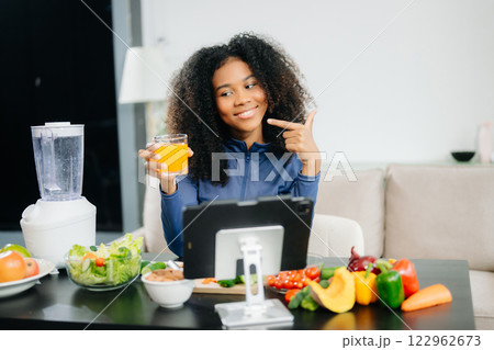 Smiling woman in a modern kitchen with fresh fruits, vegetables, blender, and orange juice, promoting clean 122962673