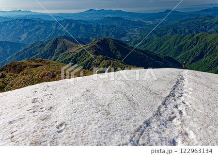 谷川岳山頂直下の雪渓を行く登山者と赤城山の眺め 122963134