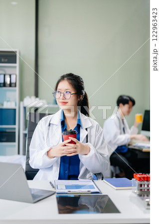 Confident young asian female doctor in white medical uniform sit at desk working on computer. Confident young asian female doctor in white medical uniform sit at desk working on computer. 122963423
