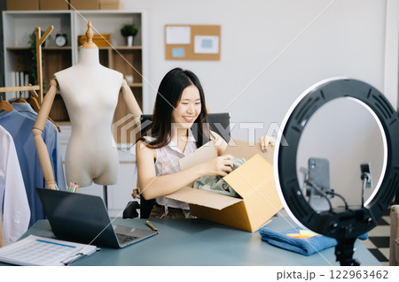 Fashion blogger concept, Young women selling clothes on video streaming.Startup small business SME, using smartphone or tablet taking receive and checking 122963462