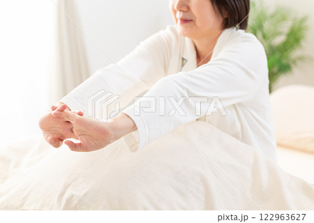 朝の寝室でストレッチをする白いパジャマ姿のミドル女性 122963627