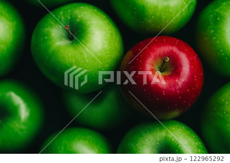 A single red apple stands out among green apples in a minimalistic setting showcasing diversity and uniqueness 122965292