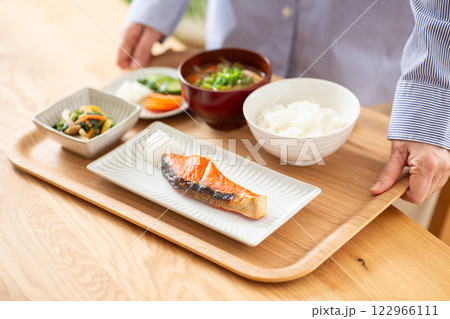 焼き鮭が並ぶ和食の朝食を配膳するミドル女性 焼き鮭が並ぶ和食の朝食を配膳するミドル女性 122966111