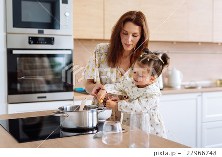 Mother, child and learning cooking with a pot Woman, girl and learning stove dinner, food and healthy food preparation at home Mother, child and learning cooking with a pot Woman, girl and learning stove dinner, food and healthy food preparation at home 122966748