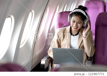 young woman is using a laptop and wireless headphones while traveling 122967772