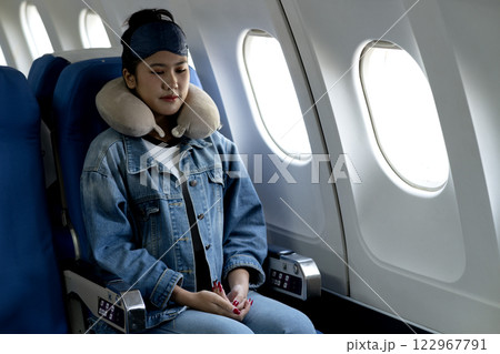 young woman travels alone on a plane and uses an eye mask 122967791