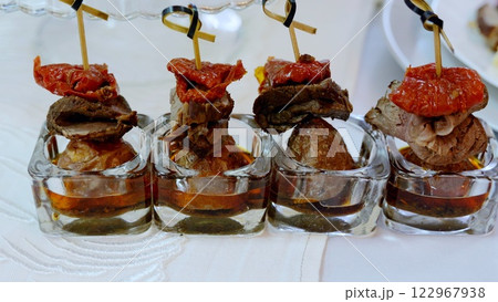 Elegant appetizers displaying roasted beef, sun dried tomatoes, and potato halves skewered, nestled in glass cups with rich savory sauce Elegant appetizers displaying roasted beef, sun dried tomatoes, and potato halves skewered, nestled in glass cups with rich savory sauce 122967938