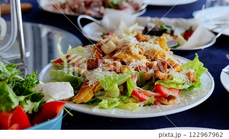 Close up caesar salad with grilled chicken, crispy croutons, ripe tomatoes, grated parmesan cheese nestled on white ceramic plate over blue linen background 122967962