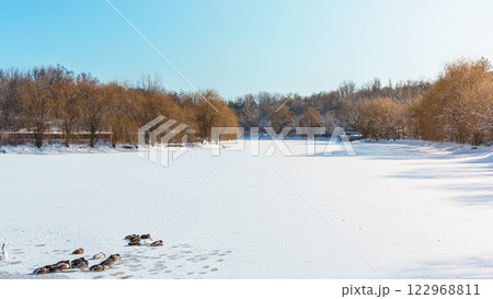Cracks on the surface of the blue ice. Frozen lake in winter mountains. It is snowing. The hills of pines. High quality photo 122968811