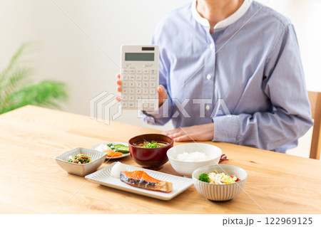 和食の朝食を前に電卓を持つミドル女性 122969125