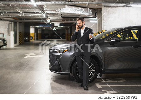Caucasian male business professional holding money and speaking on phone in underground parking garage. Dressed in formal suit, exhibiting confidence. 122969792