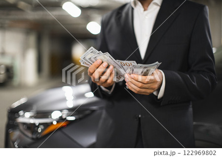Caucasian male businessman in suit counts cash money in underground parking. Image reflects finance, wealth, secrecy. Mid-adult male portrayed in professional setting, surrounded by urban environment. 122969802