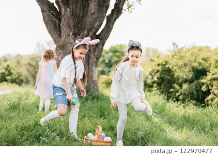 Easter egg hunt. Group Of Children Wearing Bunny Ears Running To Pick Up colorful Egg On Easter Egg Hunt In Garden. Easter tradition Easter egg hunt. Group Of Children Wearing Bunny Ears Running To Pick Up colorful Egg On Easter Egg Hunt In Garden. Easter tradition 122970477