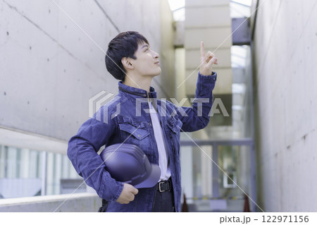 現場でヘルメットを抱えて点検する若い作業員 122971156