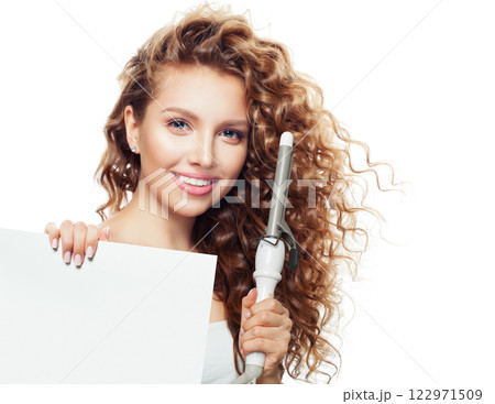 Positive brown haired woman with shiny long curly hairstyle showing curling iron.  122971509