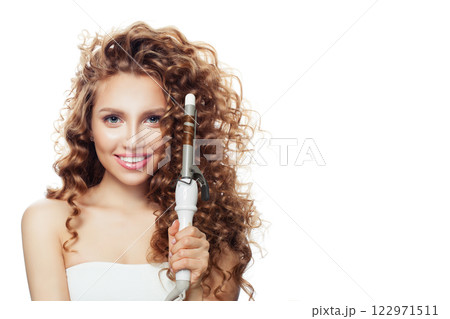 Charming brunette model using curling iron on white background.  122971511