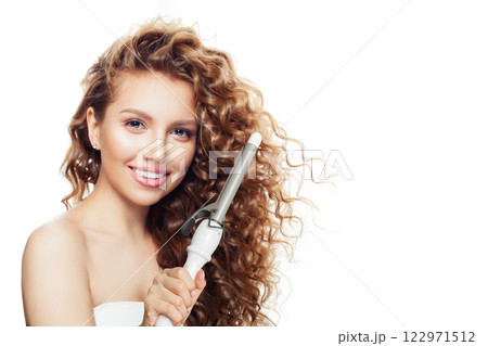 Young woman with curly hairstyle using hot curling tongs iron, indoor fashion portrait.  122971512