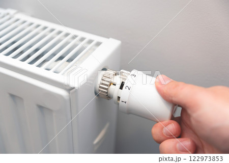 Modern white radiator, hand holding thermostat Modern white radiator, hand holding thermostat 122973853