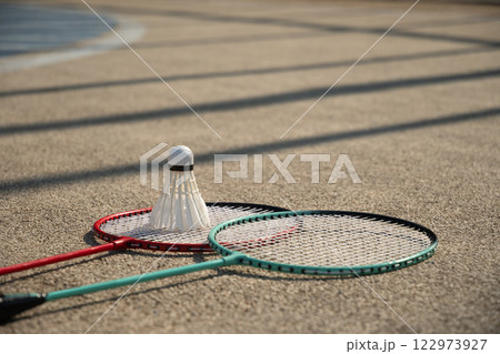 White badminton shuttlecock and badminton rackets on floor sport badminton court in sunny shadow. Outdoors. Close up. 122973927