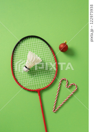Christmas badminton concept with racket, candy cane as heart, red ball and white badminton shuttlecock on green background. View from above. Xmas vertical greeting card. Christmas badminton concept with racket, candy cane as heart, red ball and white badminton shuttlecock on green background. View from above. Xmas vertical greeting card. 122973938
