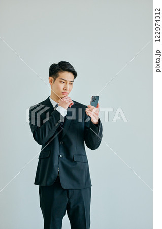 あごに手を当ててスマホを持つ20代の若い男性 122974312