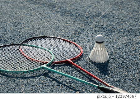 White badminton shuttlecock and two badminton rackets on blue floor sport badminton court. Outdoors. Close up. 122974367