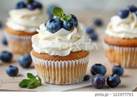 Freshly baked cupcake topped with creamy frosting, blueberries, and mint leaves. 122977701