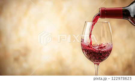 Red wine being poured into a glass against a soft beige background, ideal for alcohol advertising or beverage promotions, copy space. 122978623