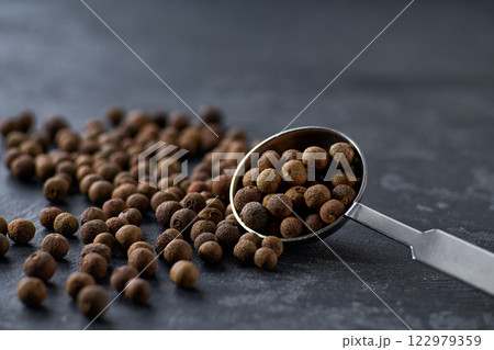 allspice or Jamaican pepper spilled from a teaspoon on a black stone table, selective focus. allspice or Jamaican pepper spilled from a teaspoon on a black stone table, selective focus. 122979359