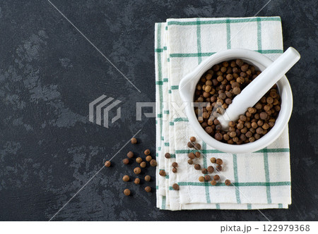 Mortar with allspice or Jamaican pepper on a black stone table, top view. 122979368