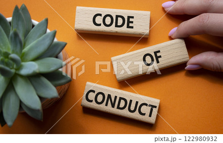 Code of conduct symbol. Wooden blocks with words Code of conduct. Businessman hand. Beautiful orange background with succulent plant. Business and Code of conduct concept. Copy space. 122980932