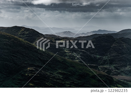 A landscape photograph showing several dark mountain ranges. The foreground displays steep slopes of dark brown and black earth. 122982235