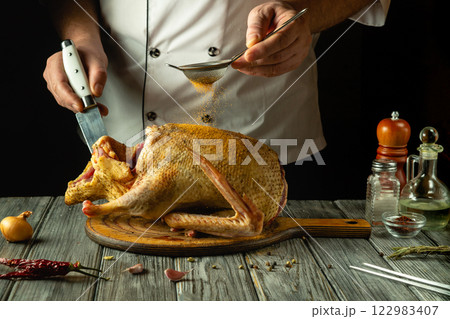 A skilled chef delicately seasons a raw duck with spices while preparing it for cooking. This culinary artistry highlights the ingredients and tools, captured in warm, inviting light A skilled chef delicately seasons a raw duck with spices while preparing it for cooking. This culinary artistry highlights the ingredients and tools, captured in warm, inviting light 122983407