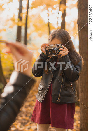Child taking picture her mother on retro camera in autumn park. Hobbies and leisure concept. 122983606