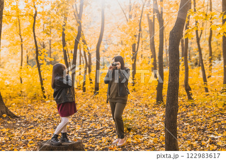 Mother taking picture her charismatic daughter on retro camera in autumn park. Hobbies and leisure concept. 122983617