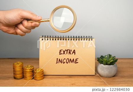 Extra income concept. Money earned in addition to a primary source of income, such as a salary or wages. notebook, magnifying glass and coins Extra income concept. Money earned in addition to a primary source of income, such as a salary or wages. notebook, magnifying glass and coins 122984030