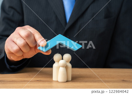 Property and family insurance concept. Miniature figures of a family stands under blue roof. Real estate and insurance agent services Property and family insurance concept. Miniature figures of a family stands under blue roof. Real estate and insurance agent services 122984042