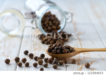 allspice or Jamaican pepper in a wooden scoop and in glass storage jar on a light kitchen table, selective focus. allspice or Jamaican pepper in a wooden scoop and in glass storage jar on a light kitchen table, selective focus. 122984655