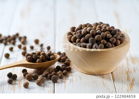 wooden bowl with allspice or Jamaican pepper seeds on a white wooden table, selective focus. wooden bowl with allspice or Jamaican pepper seeds on a white wooden table, selective focus. 122984659