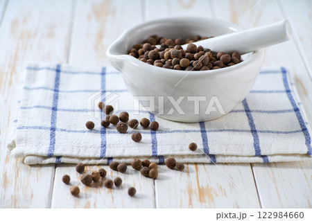 Mortar with allspice or Jamaican pepper on a white wooden table, selective focus. Mortar with allspice or Jamaican pepper on a white wooden table, selective focus. 122984660