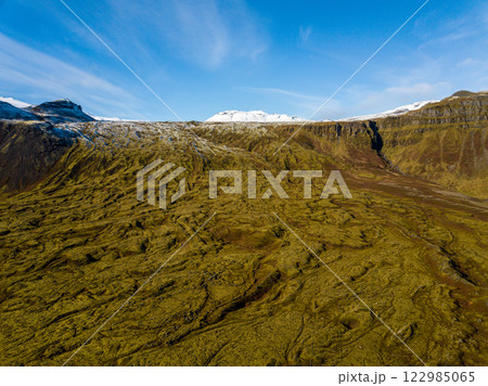 Scenic aerial shot of expansive icelandic terrain featuring snow-capped mountains and a canyon adorned with lush green moss 122985065