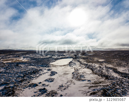 Aerial of snow covering the volcanic landscape near Dettifoss Waterfall in Iceland, creating a serene winter scene under a cloudy sky 122985087